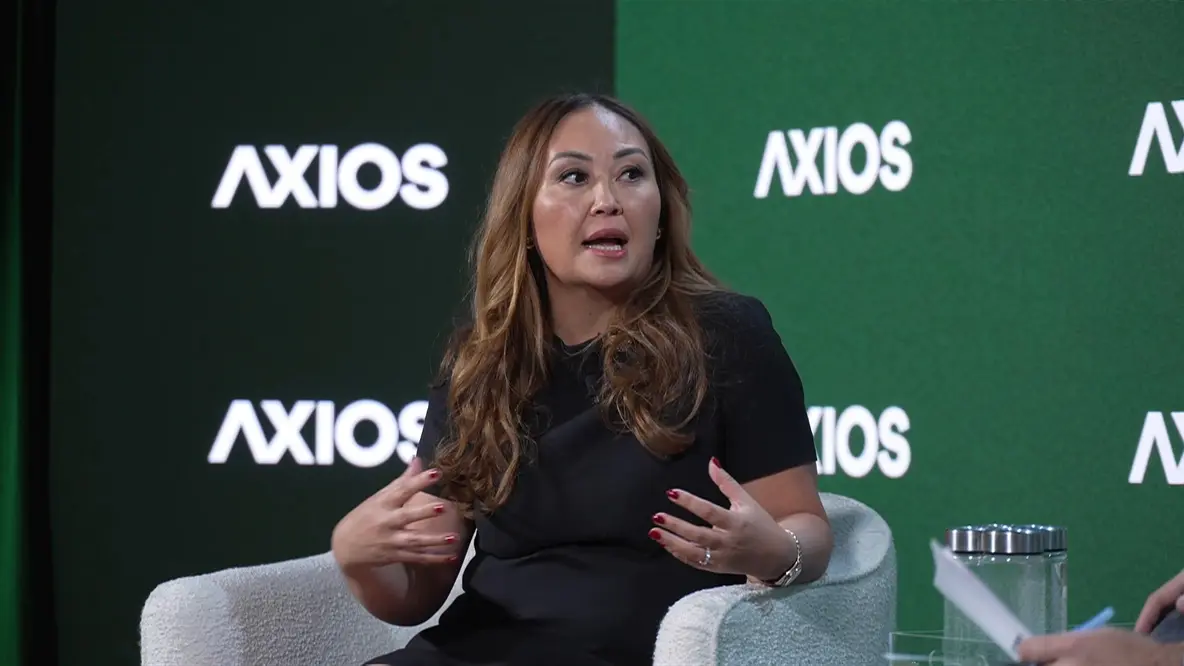 مدیر عملیات کوین‌بیس، امیلی چوی، در جلوی پس‌زمینه با لوگوی «آکسیوز» صحبت می‌کند. 