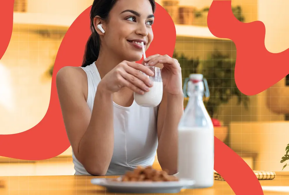 زنی لبخند می‌زند در حالی که لیوان شیری با نی در دست دارد و پشت میز نشسته است